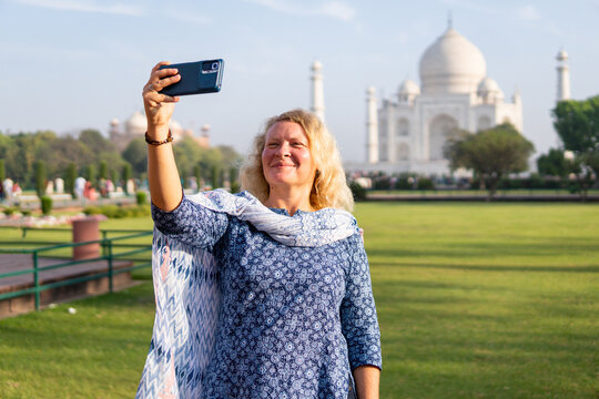 Attractive young woman taking selfie with the iconic marble white Taj Mahal mausoleum on background in Agra, Uttar Pradesh, India