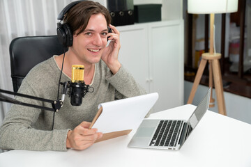 Host channel in smart broadcaster with talking show on live social media streaming with script note reading to listeners, wearing headphones to record video streamer at modern home studio. Pecuniary.