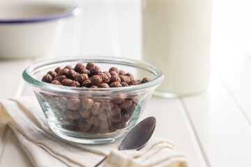 Breakfast cereal chocolate balls in bowl on white table.
