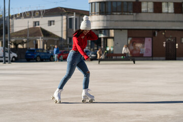 Young woman roller skating through city square, sporting red sweater, blue jeans, white beanie,...