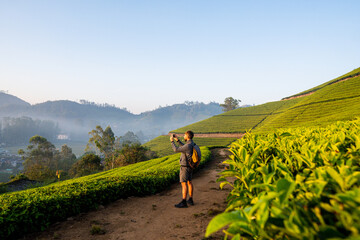 Young man with backpack taking photos of tea plantations in Munnar. Eco tourism in Kerala, India