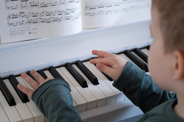 A child wearing a green sweater playing the piano while reading sheet music. This captures the learning process and love for music. 
