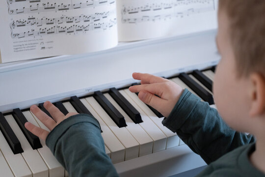 A child wearing a green sweater playing the piano while reading sheet music. This captures the learning process and love for music. 