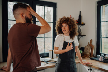 Young couple arguing in kitchen, woman explaining with hand gestures, man holding head