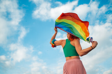 Woman holding rainbow flag celebrating lgbtq plus pride with cloudy sky