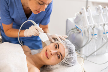 Young woman cosmetologist performs hardware facial exfoliating procedure to young female patient