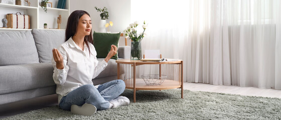 Beautiful young Asian woman meditating in living room