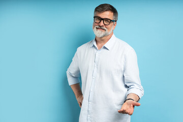 Bearded middle-aged man wearing glasses posing over blue studio background