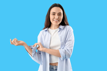 Beautiful young woman rolling up her sleeve on light blue background