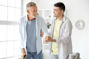 Young man helping his father to walk at home