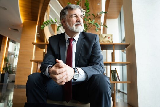 Business portrait - mature businessman sitting in office lobby. Male executive relaxing in office lounge - Powered by Adobe