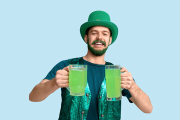 Young man in leprechaun hat with green beard holding glasses of beer on blue background. St....