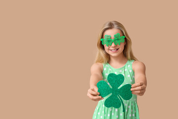 Cute little girl in decorative glasses with clover on brown background. St. Patrick's Day...