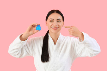 Fototapeta premium Beautiful young happy woman in bathrobe pointing at dental floss on pink background