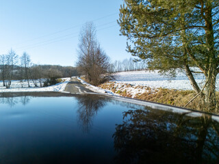 A scenic view from a car roof, capturing a peaceful winter road surrounded by trees and snow under a clear blue sky.