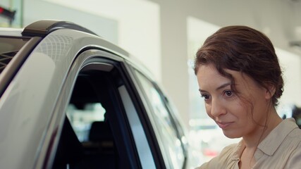 Woman in showroom looking to buy vehicle, assessing condition of cars. Customer in dealership...