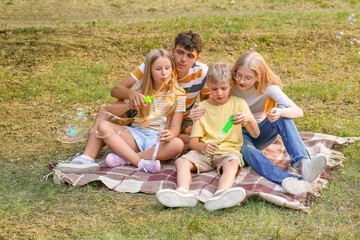 Fototapeta premium Happy family with cute children blowing soap bubbles while sitting on grass in park