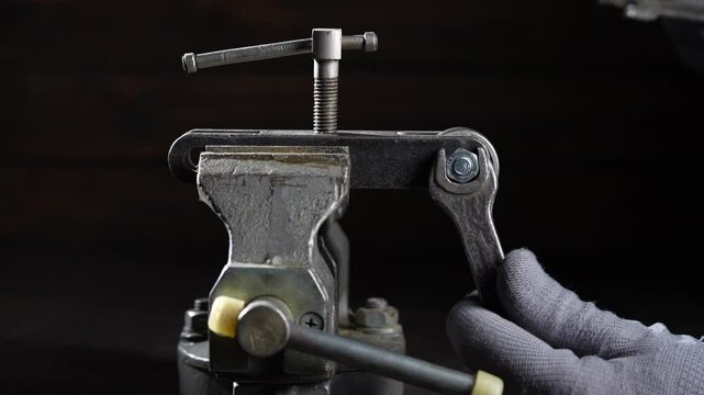 Mechanic in a workshop using a vice unscrews a nut with wrenches, close up. Using old spanner wrench and clamp to remove nut from bolt. Work of a worker at a workplace