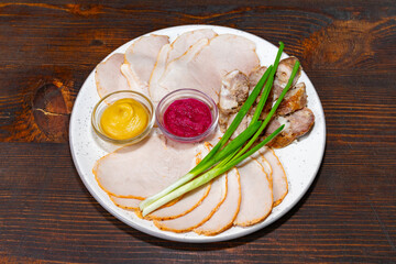 Sliced deli meats served with sauces and green onions on a plate Savory vegetable pie served with fresh garnishes on a white plate