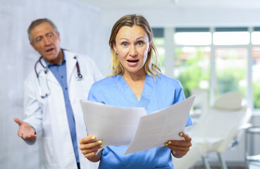 Female doctor reads paper documents report and shouts at elderly subordinate man for late provision...
