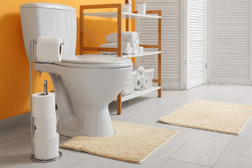 Interior of restroom with toilet bowl, shelving unit and paper holder near yellow wall