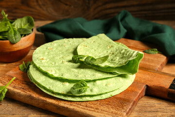 Board with round green lavash and spinach on wooden background