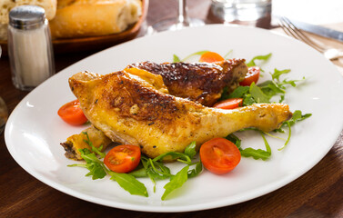 Roasted chicken legs with golden crust served with cherry tomatoes and arugula on plate