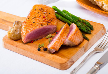 Juicy roasted duck breast served on wooden board with baked onions, pickled asparagus and spices