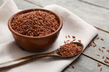 Bowl and spoon with raw brown rice on wooden background