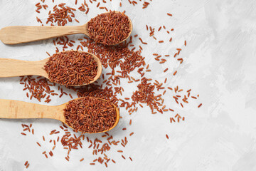 Wooden spoons with raw brown rice on white grunge background