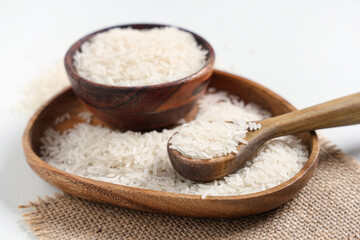Wooden plate and bowl of raw rice with spoon on white background
