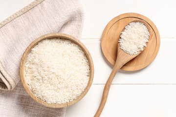 Bowl and spoon with raw rice on white wooden background