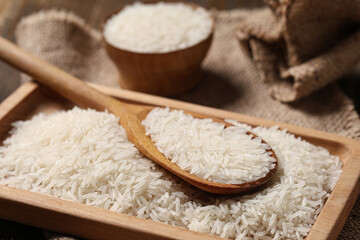 Wooden tray with raw rice and spoon, closeup