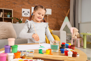 Little girl painting with brush on table at home
