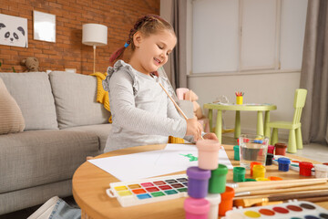 Little girl painting with brush on table at home