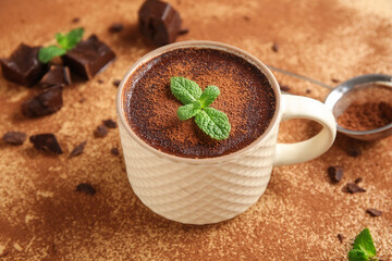 Cup of hot chocolate with mint leaves and cocoa powder on beige background