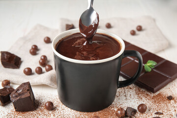 Cup of hot chocolate with balls and spoon on white wooden background