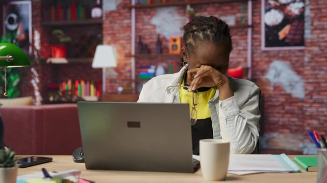 Overworked freelancer in apartment trying to relax, closing eyes after working too much on laptop. Remote worker feeling eye strain, getting overstimulated while working from home, camera B