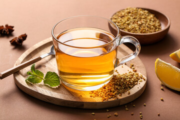 Glass cup of hot buckwheat tea with lemon slice and mint leaves on brown background