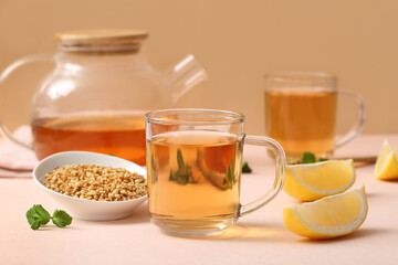 Glass cup of hot buckwheat tea with mint leaves and lemon slices on pink table