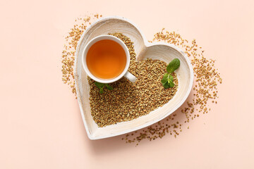 Heart shaped bowl with cup of hot buckwheat tea and mint leaves on pink background