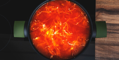 Red vegetable tomato soup with cabbage in black saucepan cook on induction hob