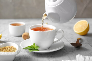 Pouring hot buckwheat tea into cup on grey grunge background