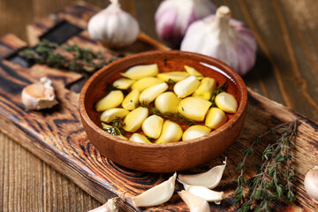 Bowl of fresh garlic oil with thyme on wooden background