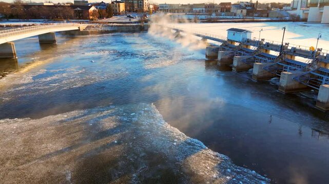 Cold waters steaming in colder air on a sub-zero Winter morning, aerial view of beautiful clashing thermals by the dam.
