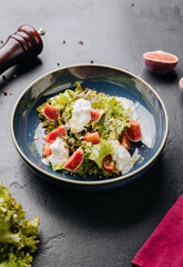 Fresh fig and burrata salad with leafy greens, almonds, and creamy dressing in a rustic blue bowl