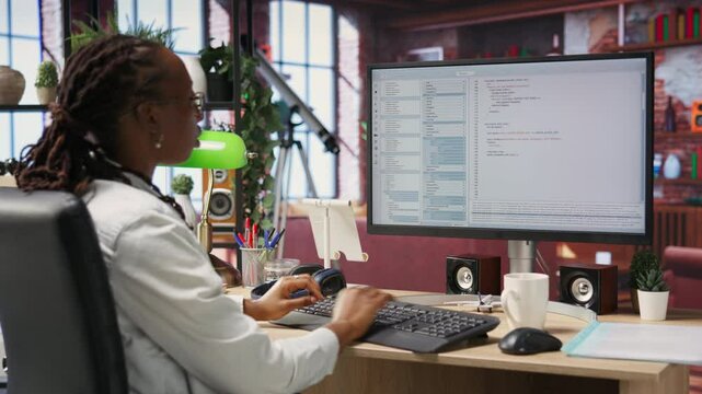 Programmer at computer desk coding, creating software, implementing algorithms. African american IT specialist in home office working with code editor, building applications, camera B