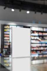 Blank tabletop sign in an acrylic holder placed on a counter in a retail store. The blurred background showcases shelves filled with colorful products, creating a perfect promotional mockup.
