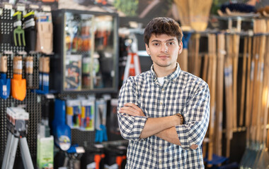 Obraz premium Guy in hardware store looks at goods on shelves, looking for modern hand tools for household chores, products with reduced price. Customer took it to hardware store and remembers shopping list