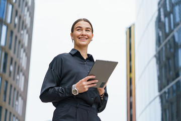 Fototapeta premium Smiling professional woman holding a tablet in an urban environment during daylight hours
